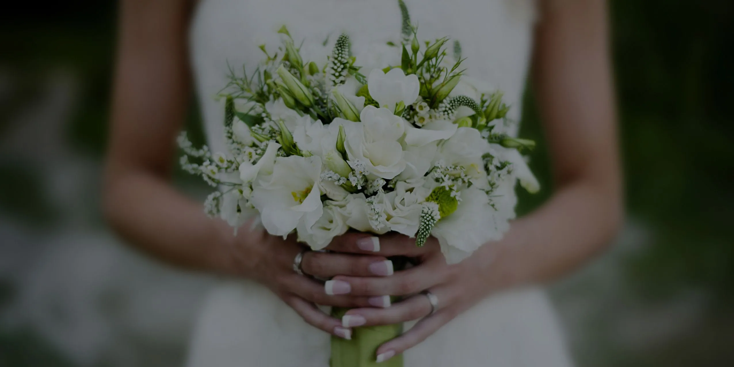 Bride in white dress holding a bouquet of white flowers and greenery.