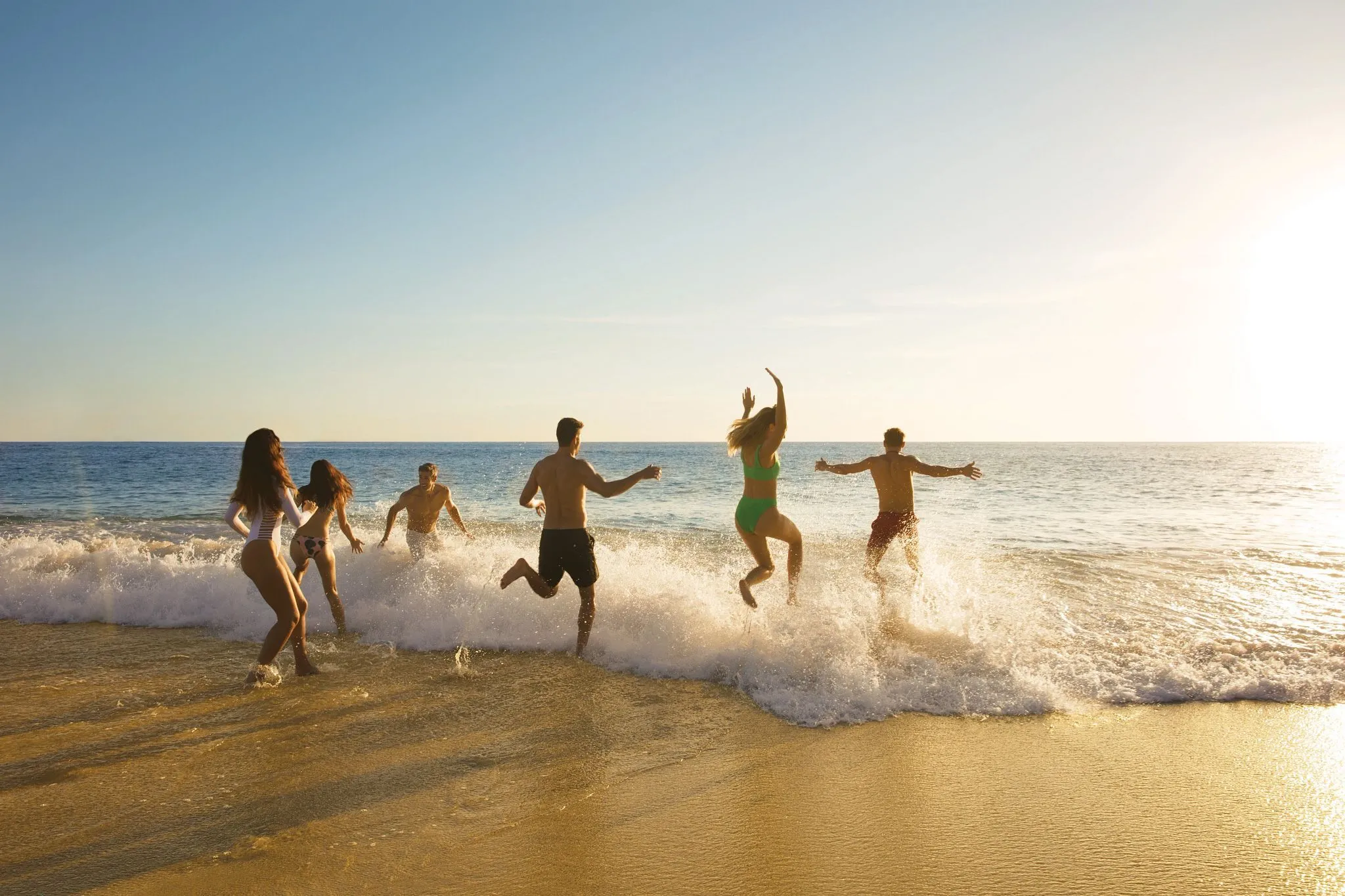 Group of friends running on beach.
