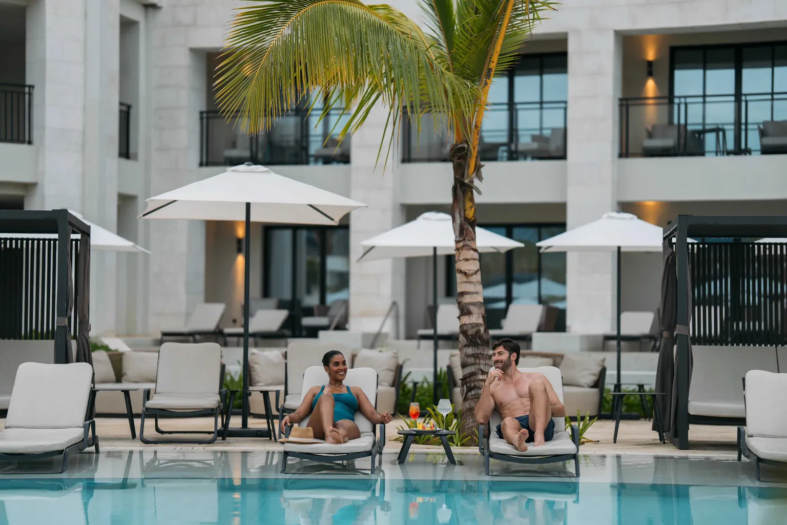 Couple relaxing poolside in loungers at Secrets Playa Esmeralda in Miches, Dominican Republic.