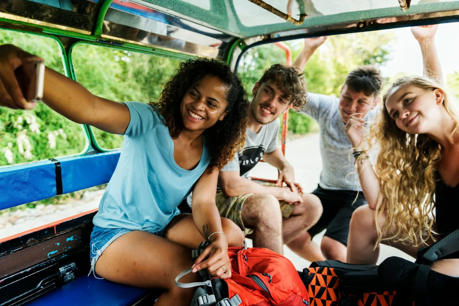 Group of young friends laughing and taking a selfie together on an open-air vehicle.