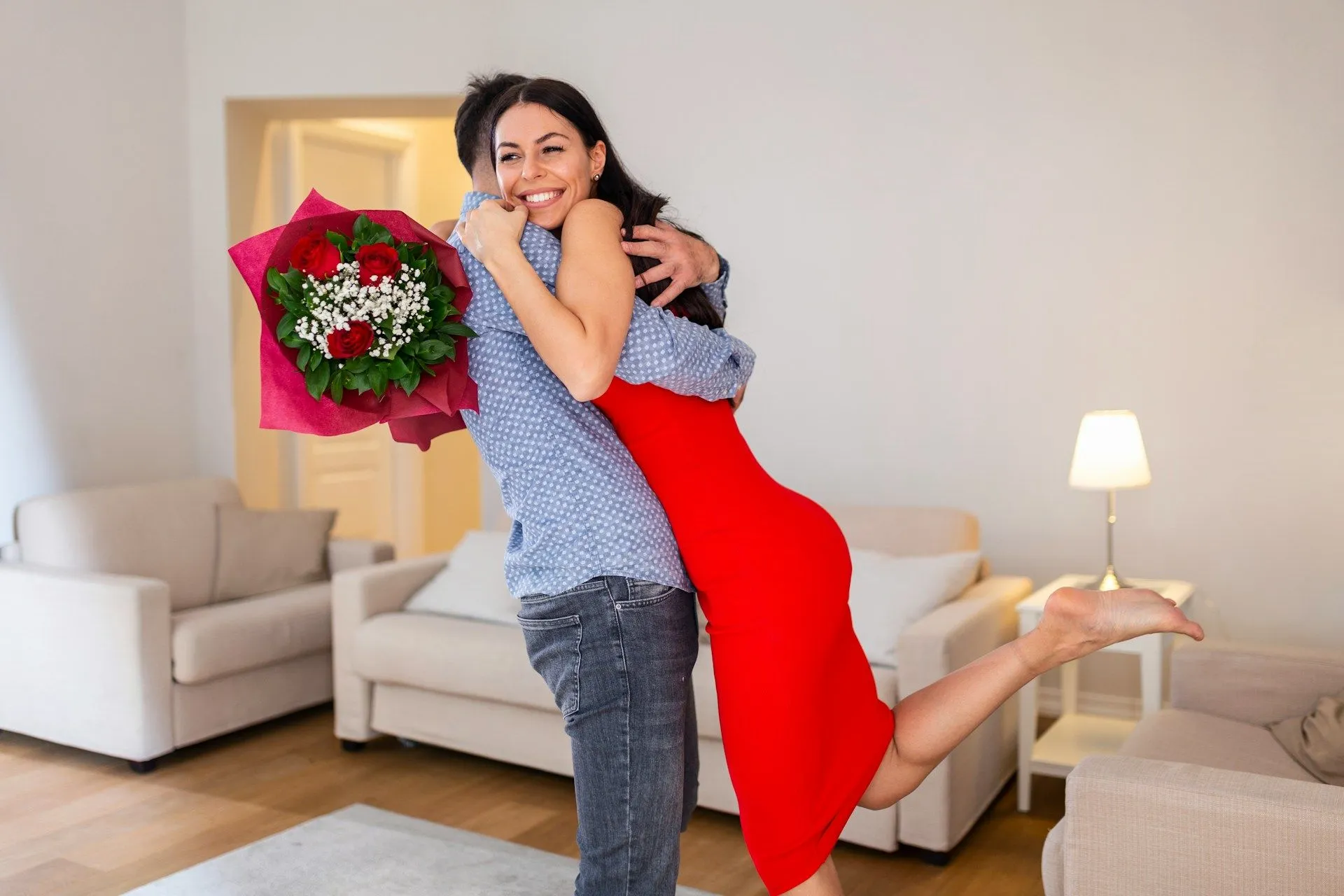 Couple hugging indoors, one holding a bouquet of red roses.