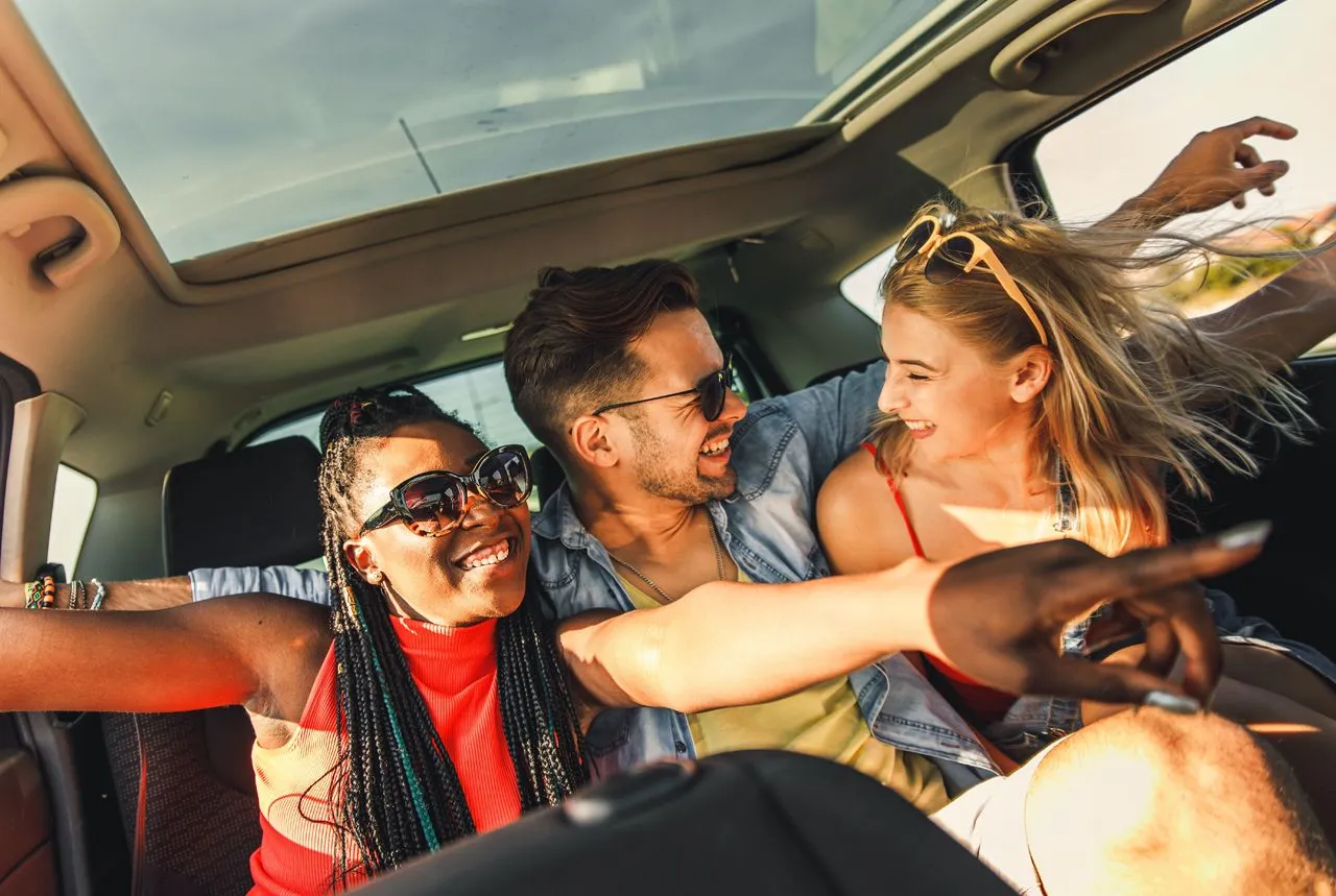 Three friends laughing together in the backseat of a car on a road trip.