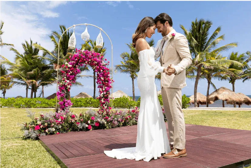 married couple embracing in front of pink flower arch and palm trees